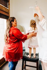 Maid of honor helping flower girl get dressed before wedding