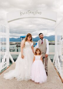 Bride and groom standing with daughter in front of Kwataqnuk gates in Polson, MT