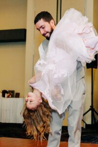 Father holding daughter upside down during father daughter dance at wedding reception