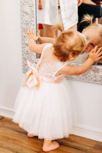 Little girl dressed up for wedding looking at herself in mirror in bridal suite at Flathead Lake Forevers