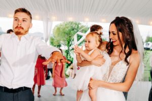 Bride, groom, and baby daughter dancing and clapping at wedding reception