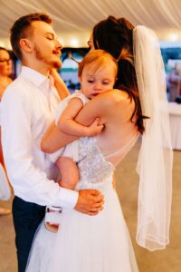 Bride and groom slow dancing with baby daughter who is falling asleep in mother's arms at Flathead Lake Forevers