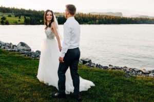 Sunset portrait of bride and groom walking together on shore of Flathead Lake at Flathead Lake Forevers