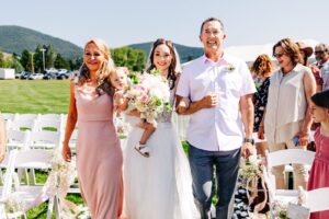 Bride walking down aisle with her parents and baby daughter at Flathead Lake Forevers