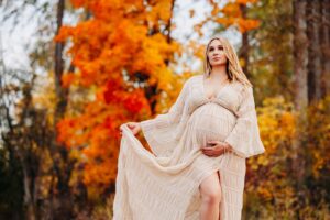 Pregnant woman standing in front of red and orange fall foliage