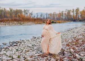 Pregnant woman standing on shore of Clark Fork River at dusk with moon