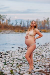 Pregnant woman in bra and underwear standing on shore of Clark Fork River