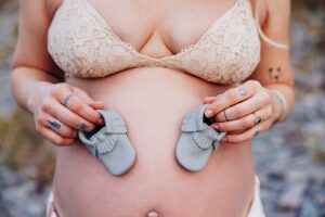 Close up photo of pregnant belly with grey baby booties