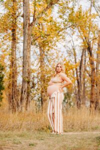 Pregnant woman in jeans and bra standing in fall forest