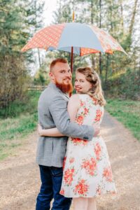 Engaged Missoula couple posing under colorful umbrella at Lincolnwood Trailhead