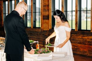 Bride and groom serving themselves dinner during indoor wedding reception