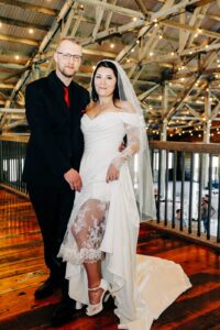 Portrait of bride showing the lace in her wedding dress, standing next to groom, upstairs at Ashley Creek Historic Venue