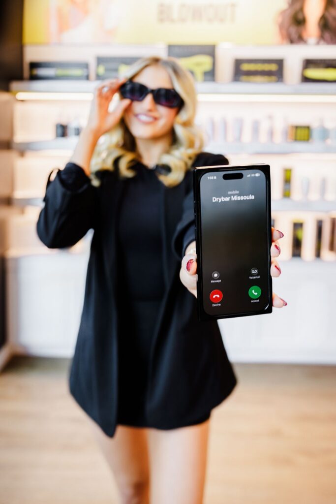 Drybar Missoula staff in sunglasses holds cell phone out with phone call from Drybar