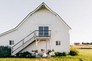 Bride and groom sitting on steps of white barn at McVey Homestead in Victor, MT