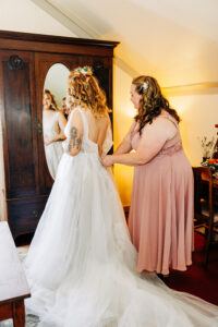 Mother zipping bride's dress in farmhouse at McVey Homestead