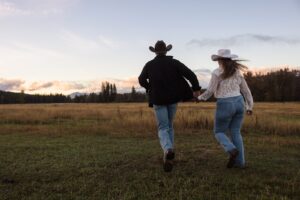 Engaged couple holding hands and running in a meadow at sunset at Lazy Sousa Ranch in Huson, MT