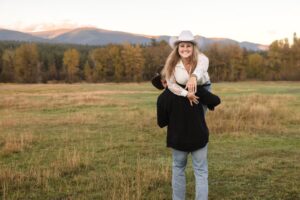 Woman being carried on man's shoulder holding out our hand with engagement ring