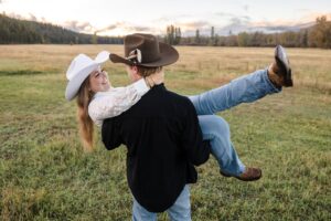 Man carrying fiance in large open field at sunset at Lazy Sousa Ranch in Huson, MT