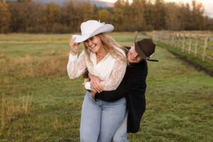 Engaged couple playful embrace in meadow at Lazy Sousa Ranch in Huson, MT