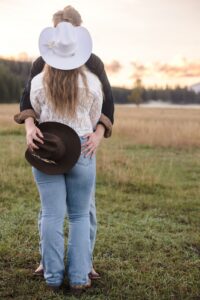 Man and woman in Western attire embracing in meadow at sunset